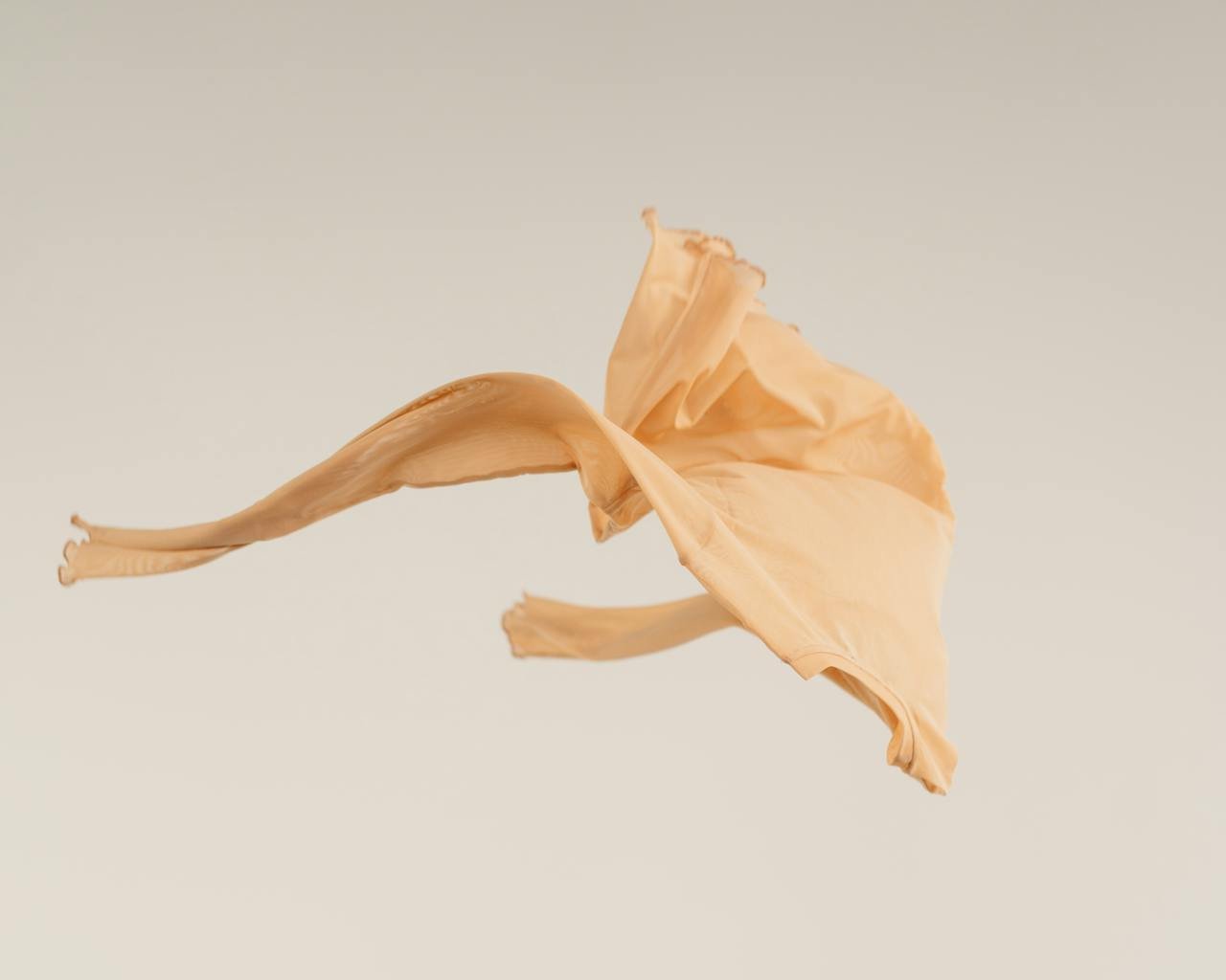 Soft beige fabric caught in motion against a clean white background, showcasing smooth texture and flowing movement.
