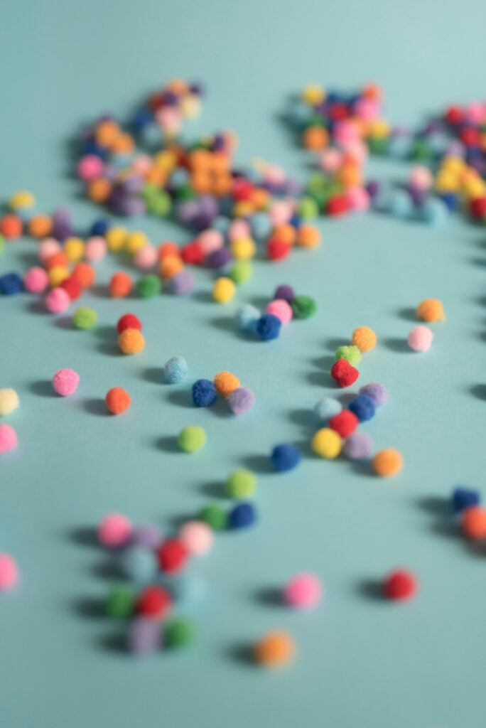 Vibrant multicolored pom poms spread on a light blue background creating a playful pattern.
